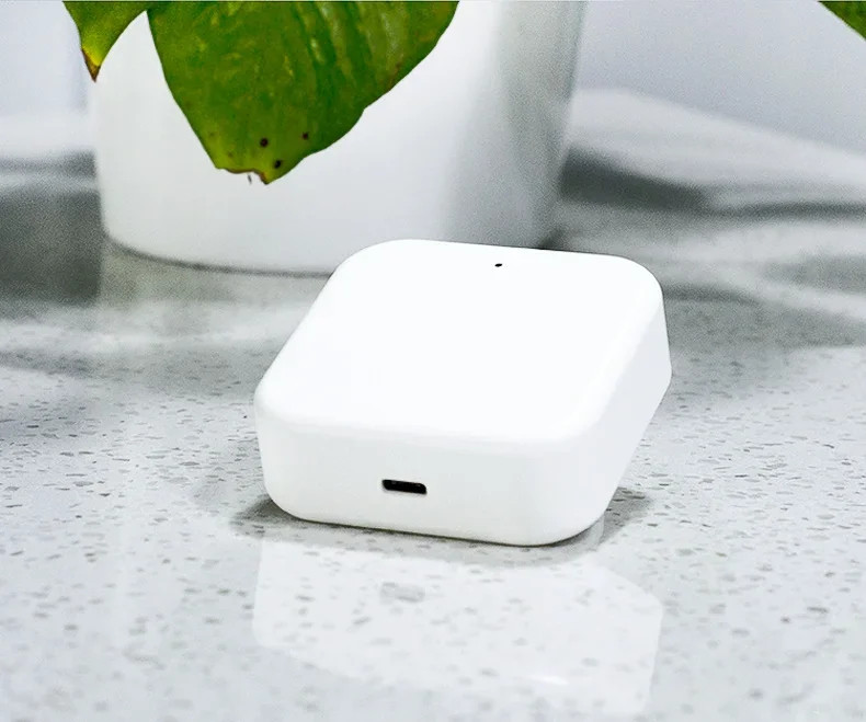 Modern fehér IoT eszköz USB-C porttal és zöld növénnyel a háttérben.